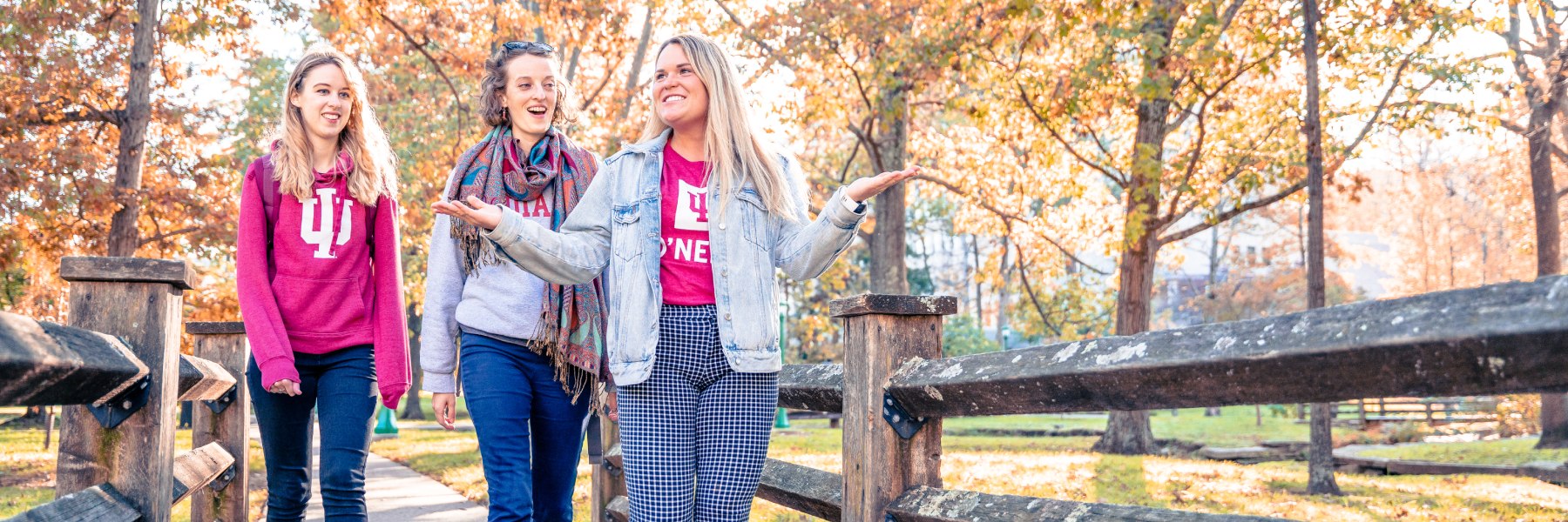 Three students on pedestrian bridge with fall colors
